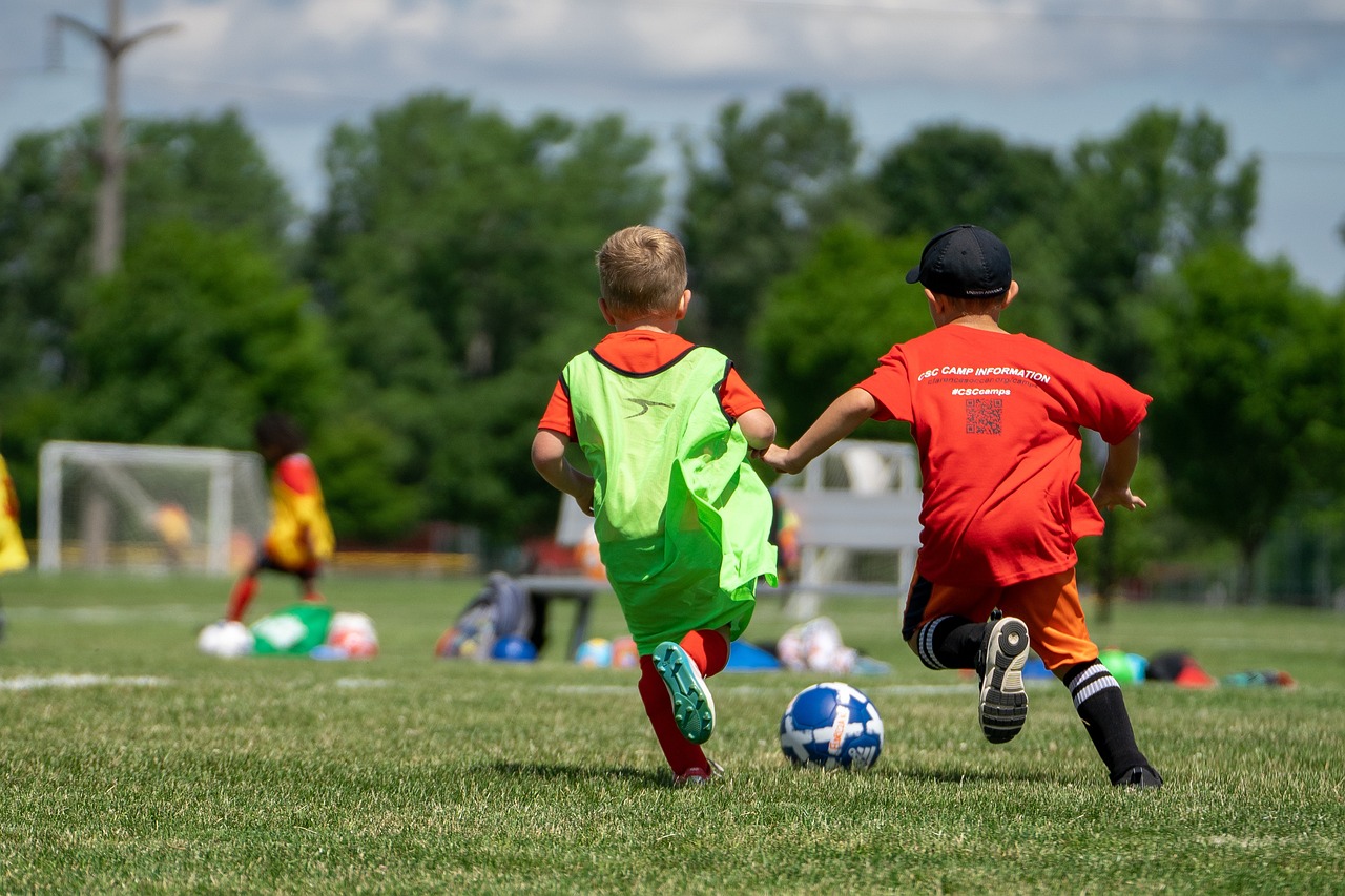 Deux jeunes enfants jouant au football sur un terrain en herbe, vêtus de maillots colorés, lors d'un match ou d'un entraînement en plein air